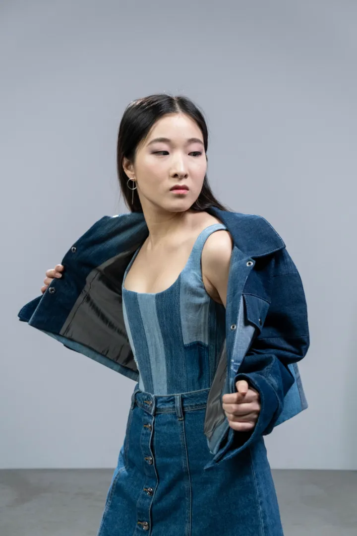Model membuka jaket denim biru tua, memakai bustier tambal dan rok denim berkancing