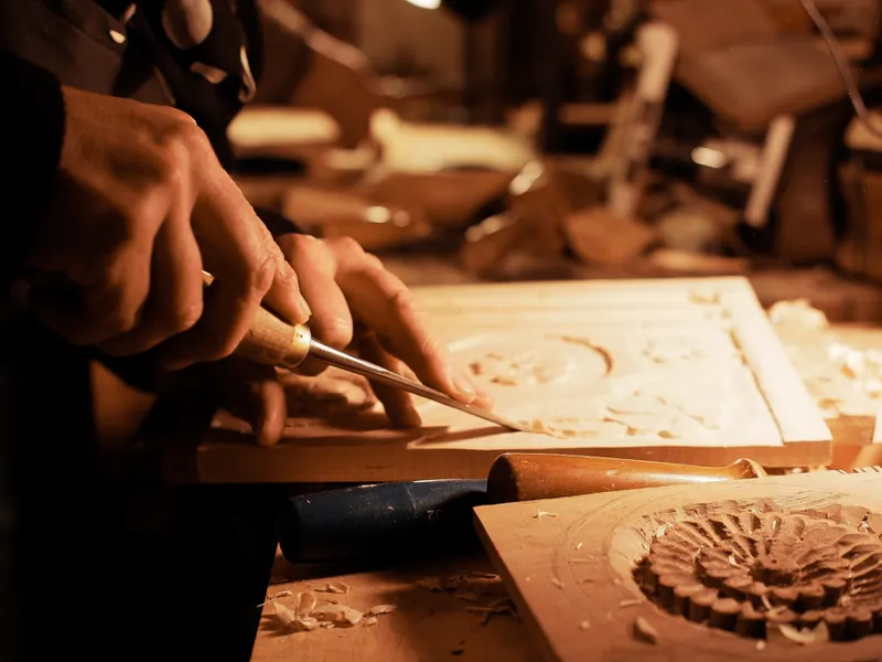 A craftsman carving a floral panel with a chisel, wood shavings on the bench