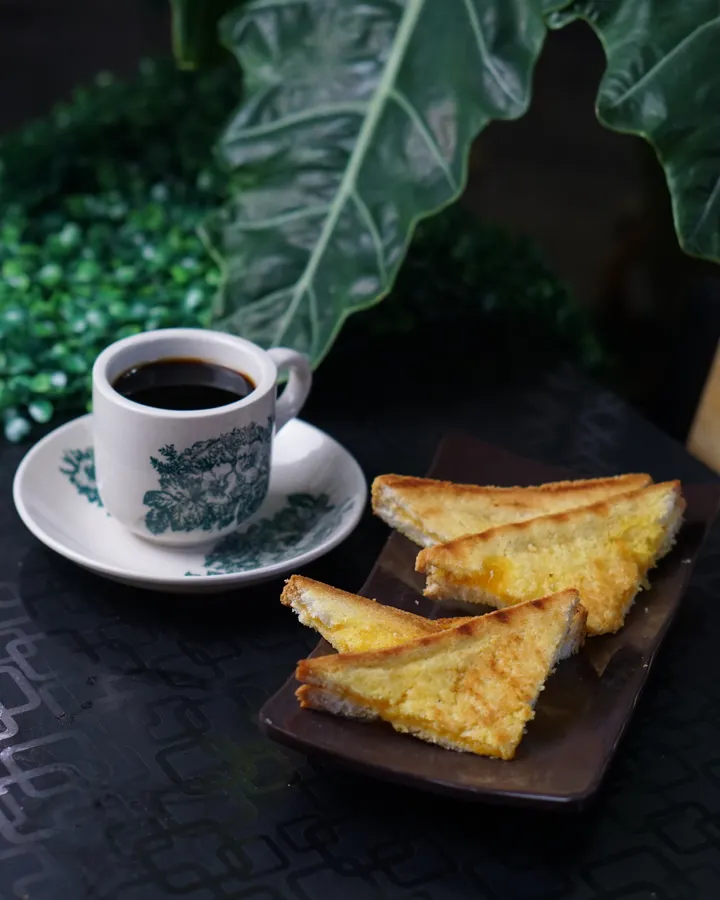 Roti bakar srikaya dipotong segitiga di samping secangkir kopi hitam