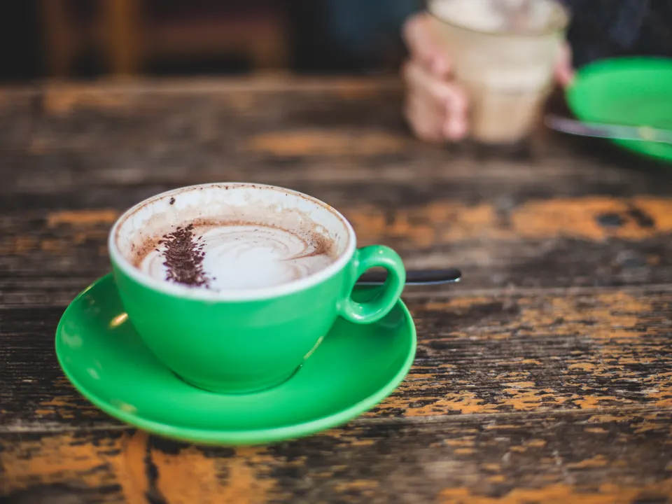 Cappuccino dalam cangkir hijau di atas meja kayu tua