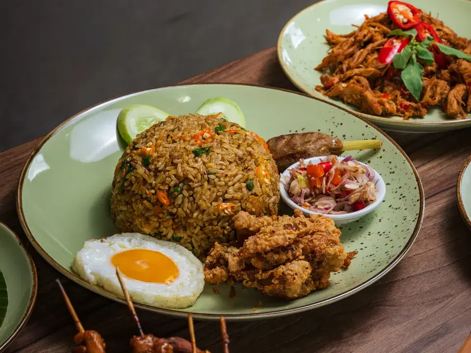 Nasi goreng dengan telur ceplok, ayam goreng, dan sate di piring hijau berbintik