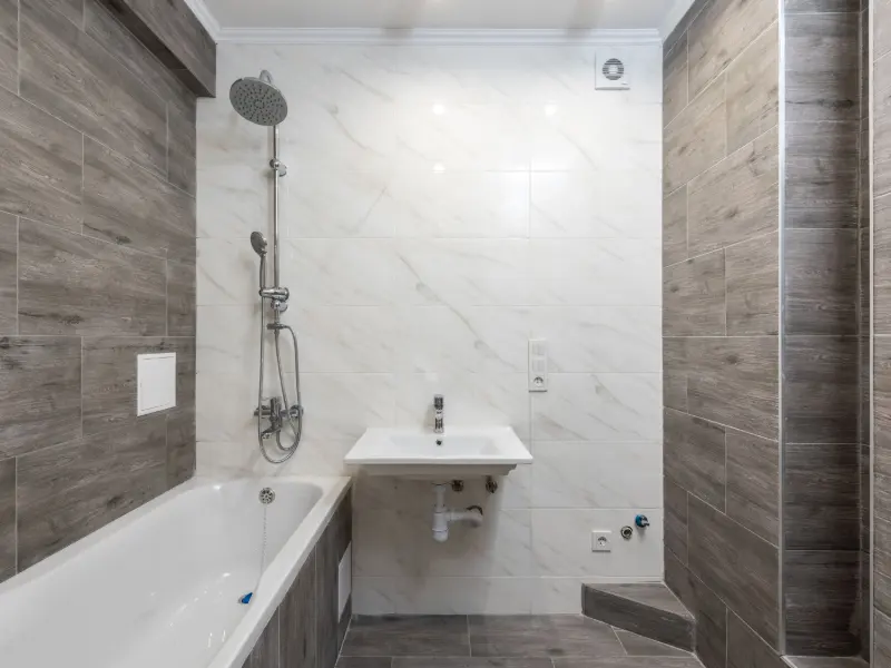 Kamar mandi dengan bak rendam, dinding marmer putih, dan keramik motif kayu abu di sisi shower