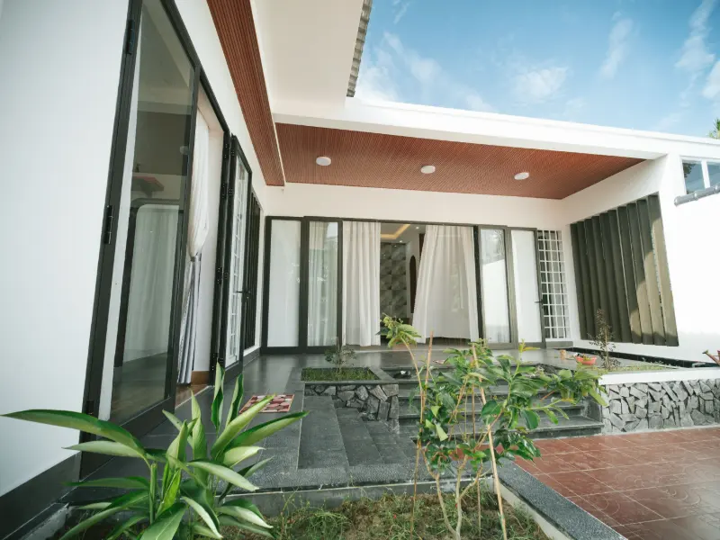 Teras belakang dengan plafon motif kayu, pintu kaca besar, lantai batu abu, dan taman kecil