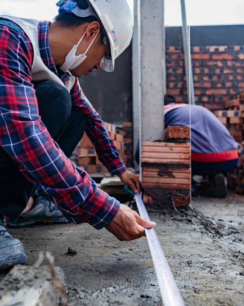 Petugas berhelm mengukur panjang lantai dengan meteran di lokasi proyek