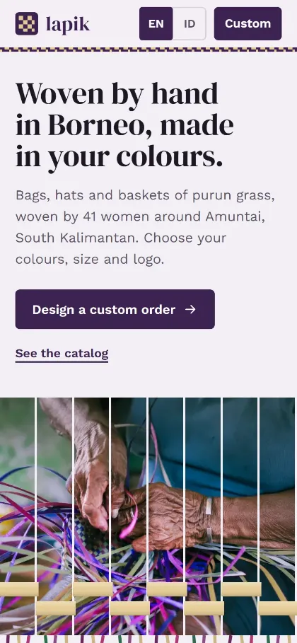 Tampilan HP demo website kerajinan anyaman Lapik: judul Woven by hand in Borneo, made in your colours, tombol EN/ID, tombol Design a custom order, dan foto tangan pengrajin menganyam bilah purun ungu yang tersusun seperti bilah anyaman